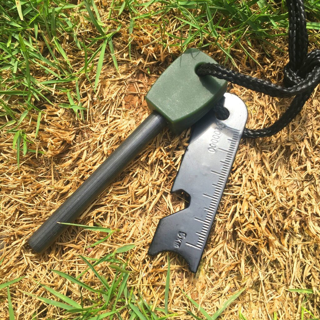 Olive drab green bushcraft fire starter kit from a ferro rod bulk FRC53 wholesale supplier, placed on natural grass and wood backdrop.