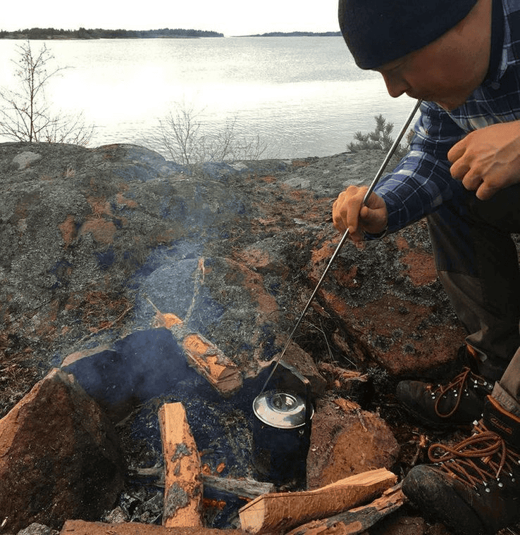 Outdoor enthusiast using the FRC22 telescopic bellow to revive a campfire, demonstrating safe fire-starting distance for wholesale fire starter kit bundles.