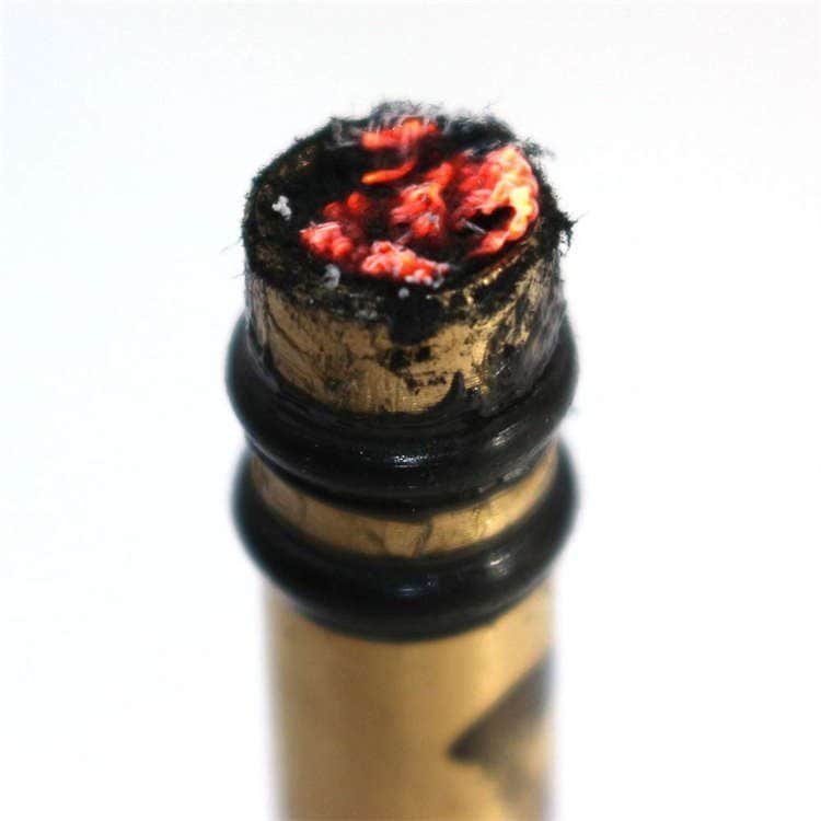 Ignited char cloth on the tip of a brass FRC16 piston, showcasing the reliable heat generation of our bulk fire steel and piston alternatives.