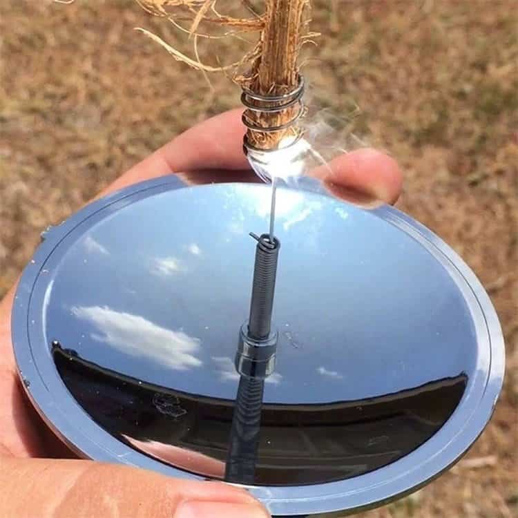 Hand holding a 3.8-inch silver solar spark lighter from the ferro rod bulk FRC29 line, concentrating sunlight to ignite tinder on a sunny day.