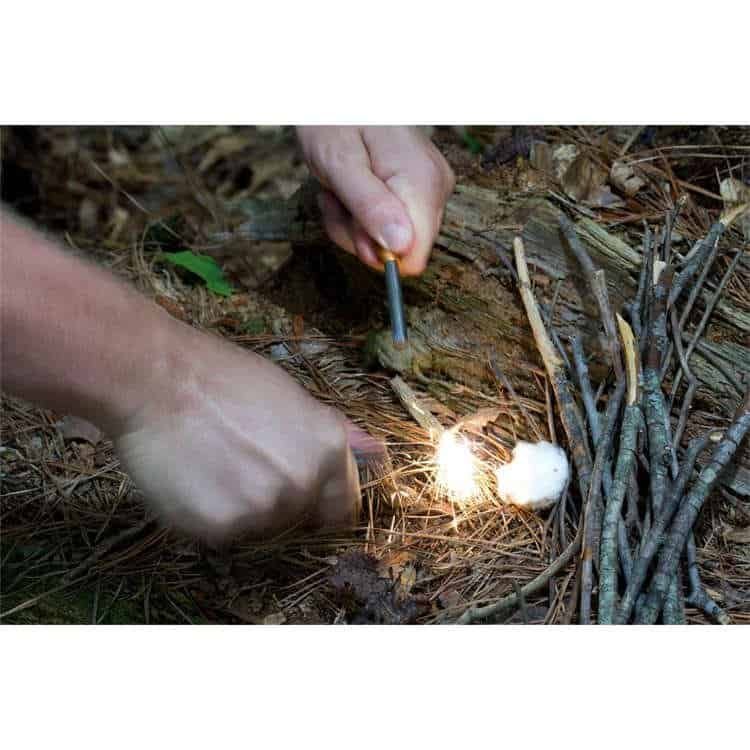 Hand striking the bulk ferrocerium rods in the forest to ignite a campfire, showcasing high-heat sparks and all-weather survival performance.