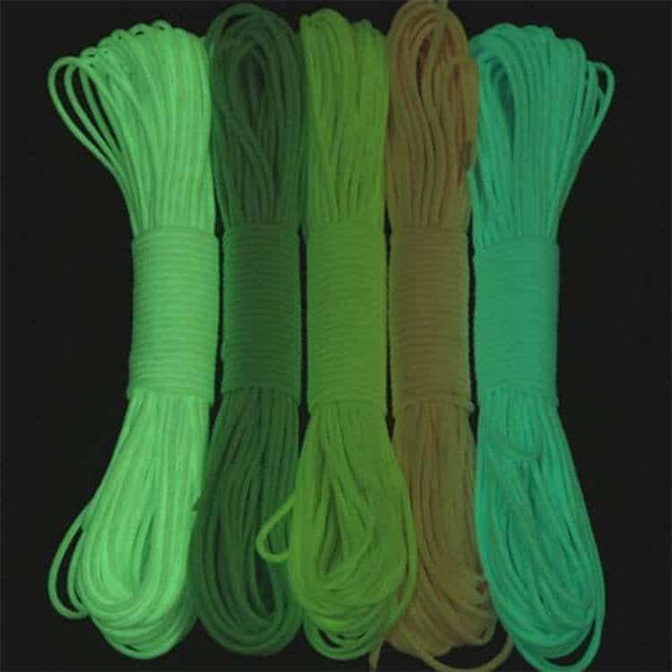 Five bundles of bulk paracord glowing in various shades of green and aqua in the dark, showcasing high-visibility photo-luminescent properties.