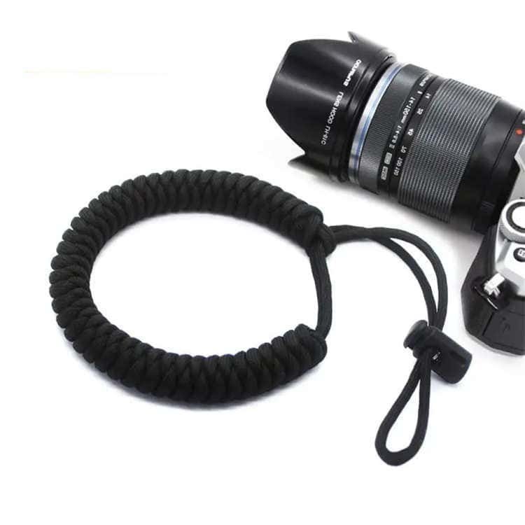 Solid black PL05 paracord camera wrist lanyard next to camera lens available in paracord lanyard bulk