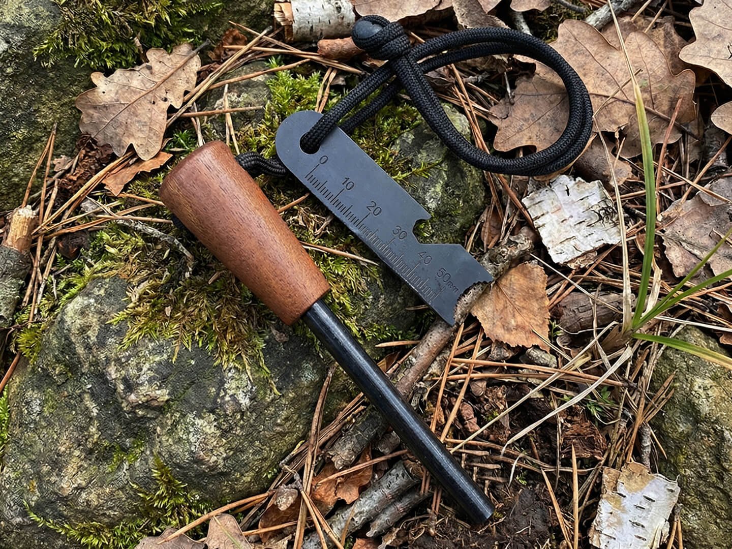 Wood handle ferro rod with ruler scraper on a mossy rock outdoors