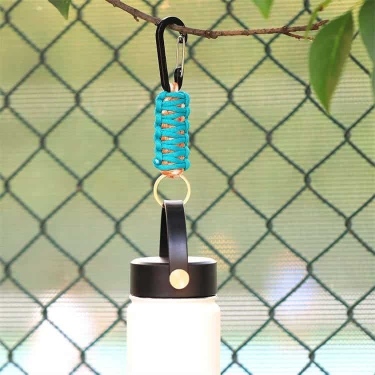 Turquoise PK03 tactical paracord keychain suspending a water bottle from a branch outdoors.